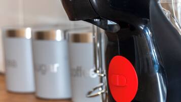 A coffee machine with a red button, a black base, and a transparent container in the background.