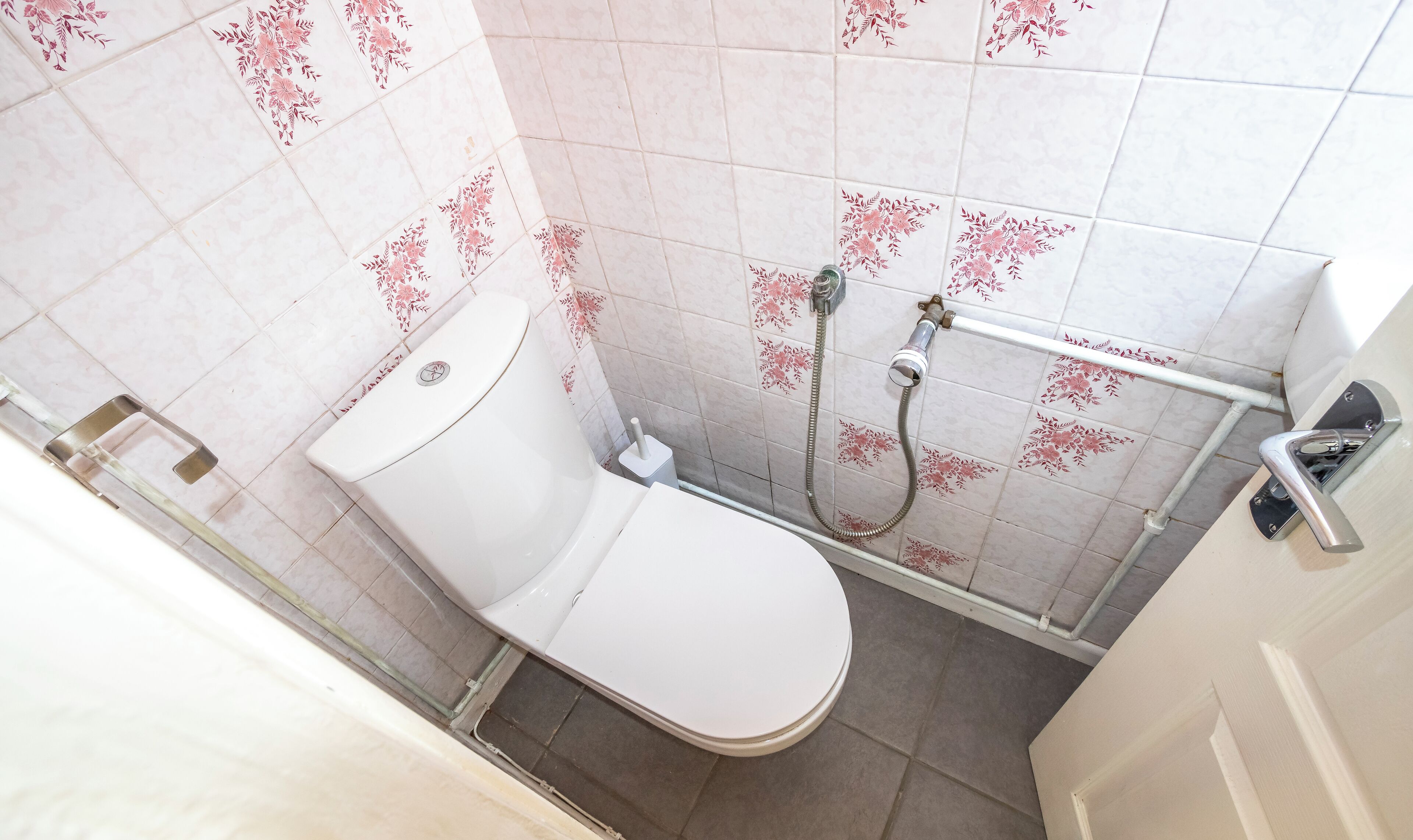 A small bathroom with a toilet, a shower, and a handrail.