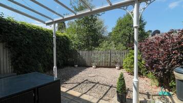 Ein überdachter Patio-Bereich mit einer Pergola, Sitzgelegenheiten und Kübelpflanzen.