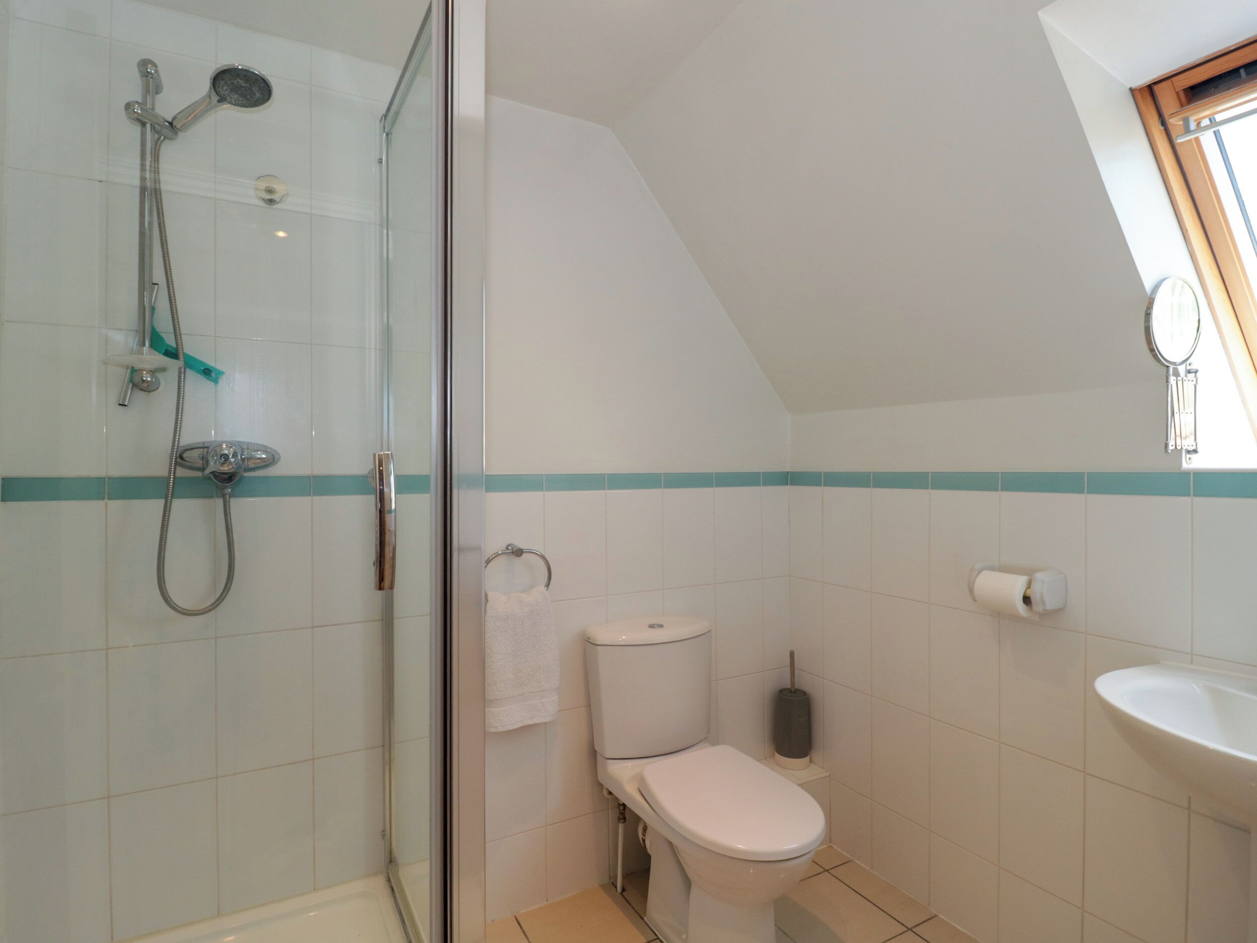 Ein Badezimmer mit Duschkabine, Toilette, Waschbecken und Fenster für Tageslicht.