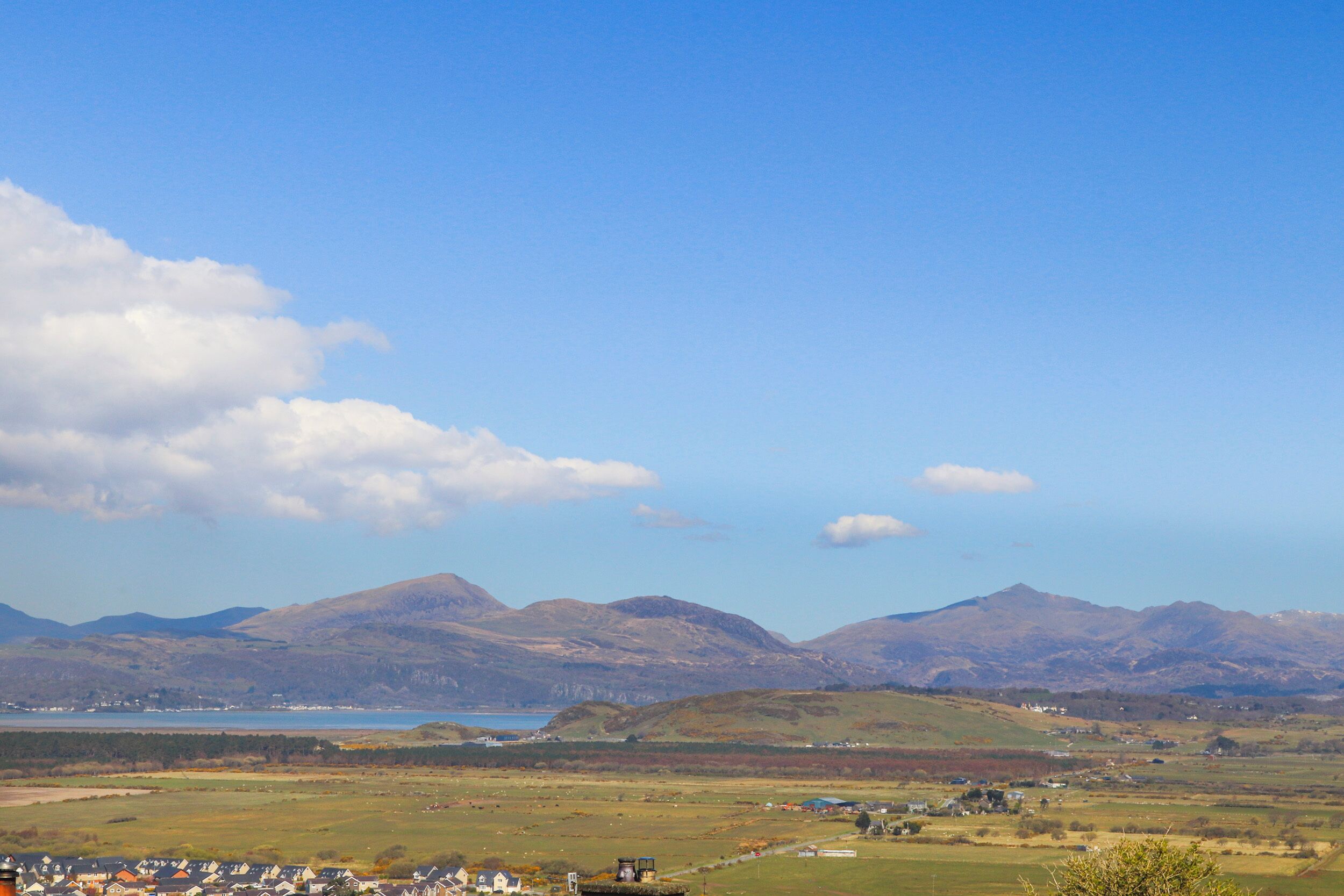 A coastal landscape with rolling hills, a small settlement, and a body of water in the distance.