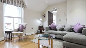 Un salon moderne avec un canapé gris, un fauteuil à motifs et une table basse en verre.
