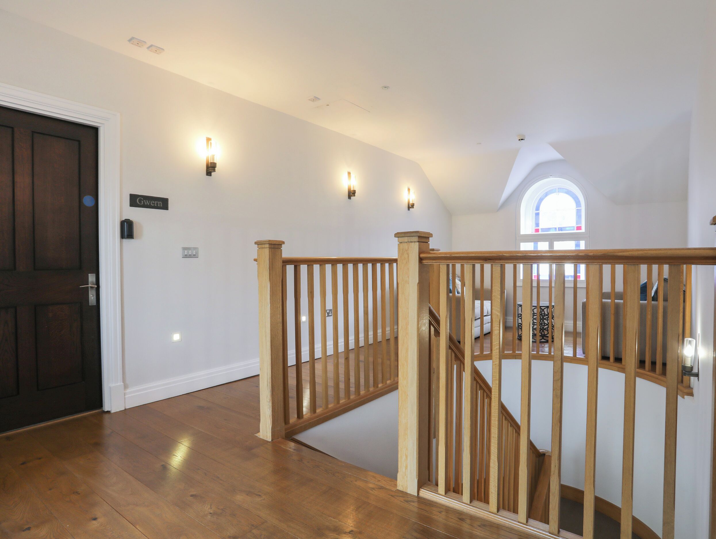 Un escalier en bois, doté d’une rampe, mène à un niveau supérieur. Une porte portant l’inscription « Gwen » est visible sur la gauche.
