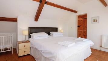 A bedroom with a large bed, wooden beams on the ceiling, a white crib, and a wooden door.