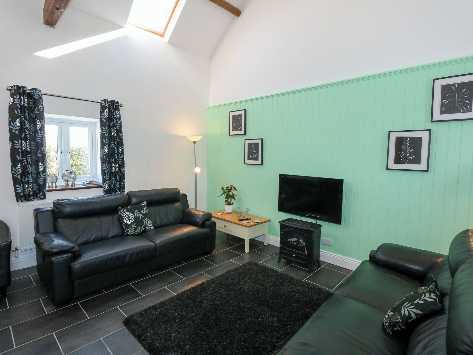 A modern living room with a black leather sofa, a flat-screen TV, and a green accent wall.
