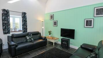 A modern living room with a black leather sofa, a flat-screen TV, and a green accent wall.
