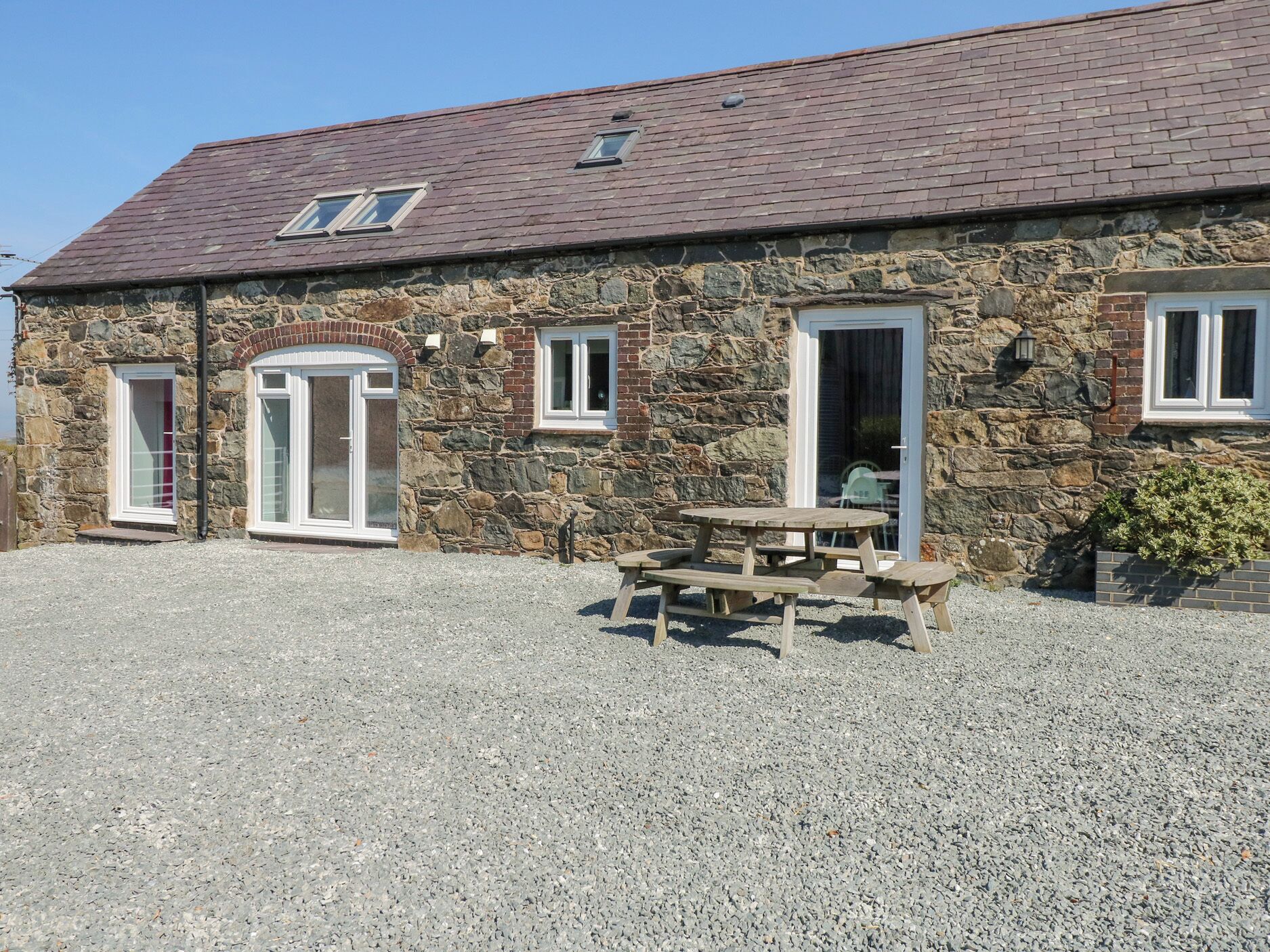 A stone building with a gravel driveway and a wooden picnic table.