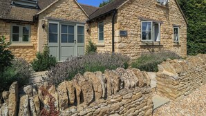 A stone building with a grey door and windows, surrounded by a stone wall and plants. - 12 Manor Farm Close (Chipping Norton)
