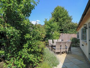 A patio with a table and chairs, surrounded by greenery and a wooden fence. - 12 Manor Farm Close (Chipping Norton)