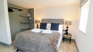A bedroom with a bed, two bedside tables, a wall-mounted shelf, and a window. - 12 Manor Farm Close (Chipping Norton)