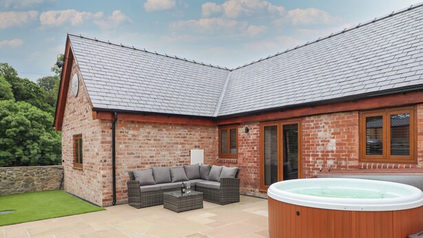A patio area with a hot tub, outdoor seating, and a brick building. - The Clockhouse (Montgomery)