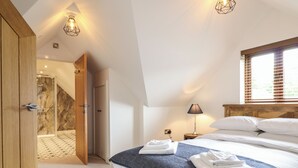 A bedroom with a bed, a bedside table, a lamp, and a window with blinds. - The Clockhouse (Montgomery)
