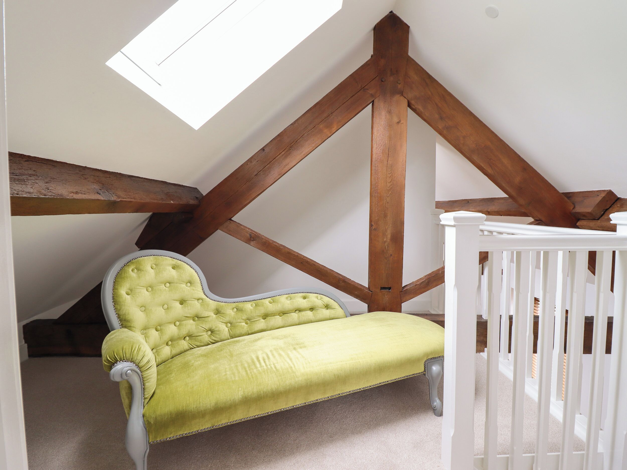 A room with a sloped ceiling, exposed wooden beams, a green upholstered chair, and a white crib.