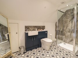 Uma casa de banho moderna com lavatório de mármore, armários escuros, sanita e cabine de duche com vidro.