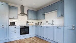 A modern kitchen with light blue cabinets, a stainless steel range hood, a microwave, and a built-in oven. - 4 Llain yr Eglwys (Newport)