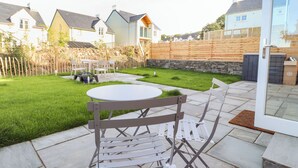 A patio with a round table and chairs, a stone pathway, and a grassy lawn. - 4 Llain yr Eglwys (Newport)