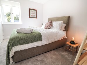 A neatly made bed with a green throw, white bedding, and a small bedside table with a lamp.
