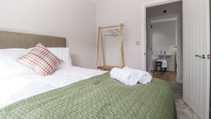 A neatly made bed with a green patterned bedspread, a white pillow with a polka dot design, and a wooden chair with a mirror. - 4 Llain yr Eglwys (Newport)