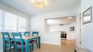 A modern kitchen with white cabinets, a built-in oven, and a microwave. There is a dining area with a wooden table and teal chairs. - 3BR/2BA Luke's Landing Island Home - Jensen Beach Retreat (Jensen Beach)