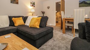 A living room with a dark grey sofa, a wooden coffee table, and a dining area with a striped chair and a small table. - 1 Springfort Cottages (Penrith)