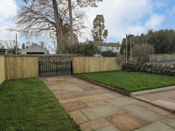 A paved patio area with stone tiles, surrounded by a wooden fence and a stone wall. - 1 Springfort Cottages (Penrith)
