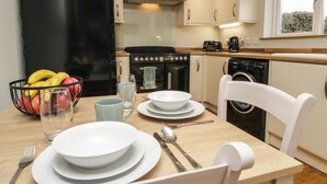 A compact kitchen with white cabinets, a black stove, a washing machine, and a dining table set with plates, bowls, and utensils. - 1 Springfort Cottages (Penrith)