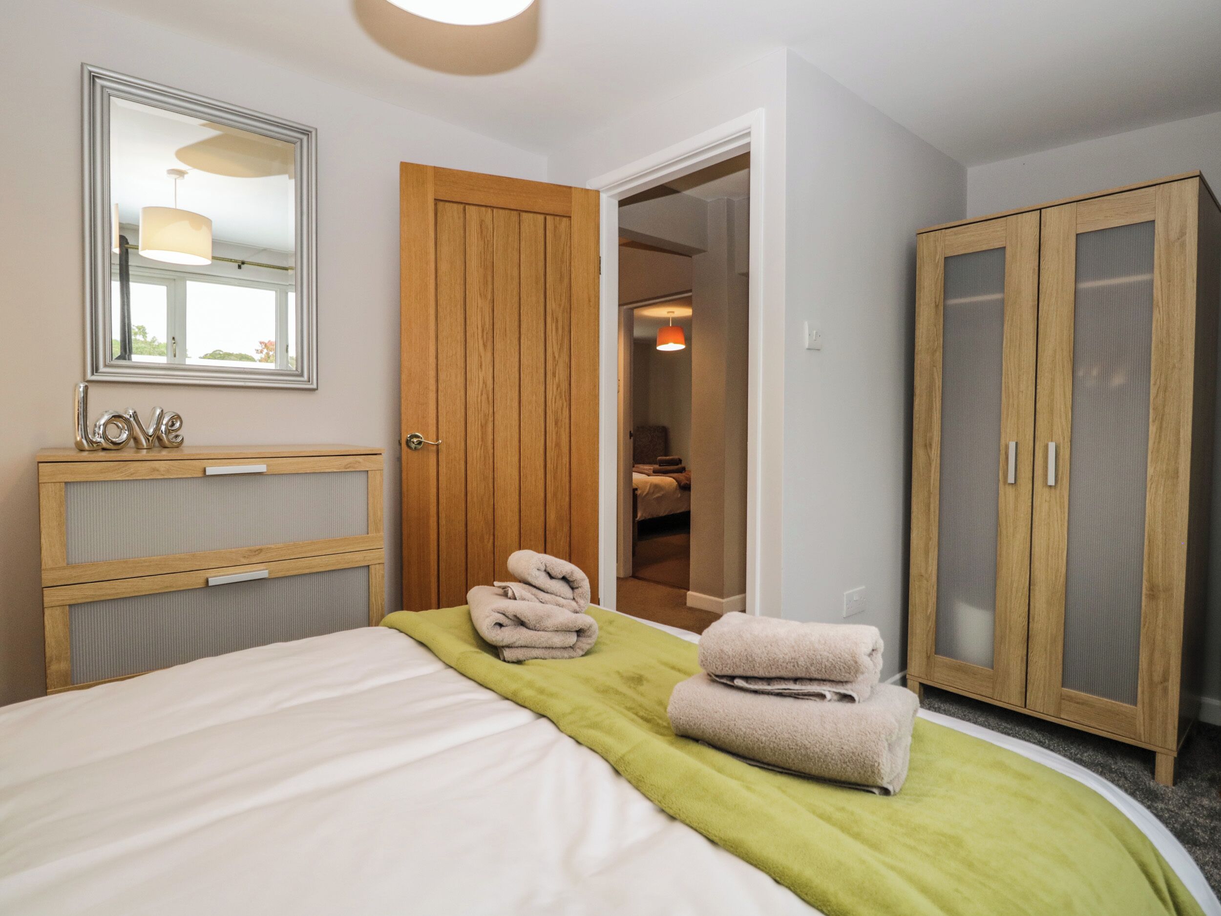 A hotel room with a bed, a wooden wardrobe, a mirror, and a door leading to another room.