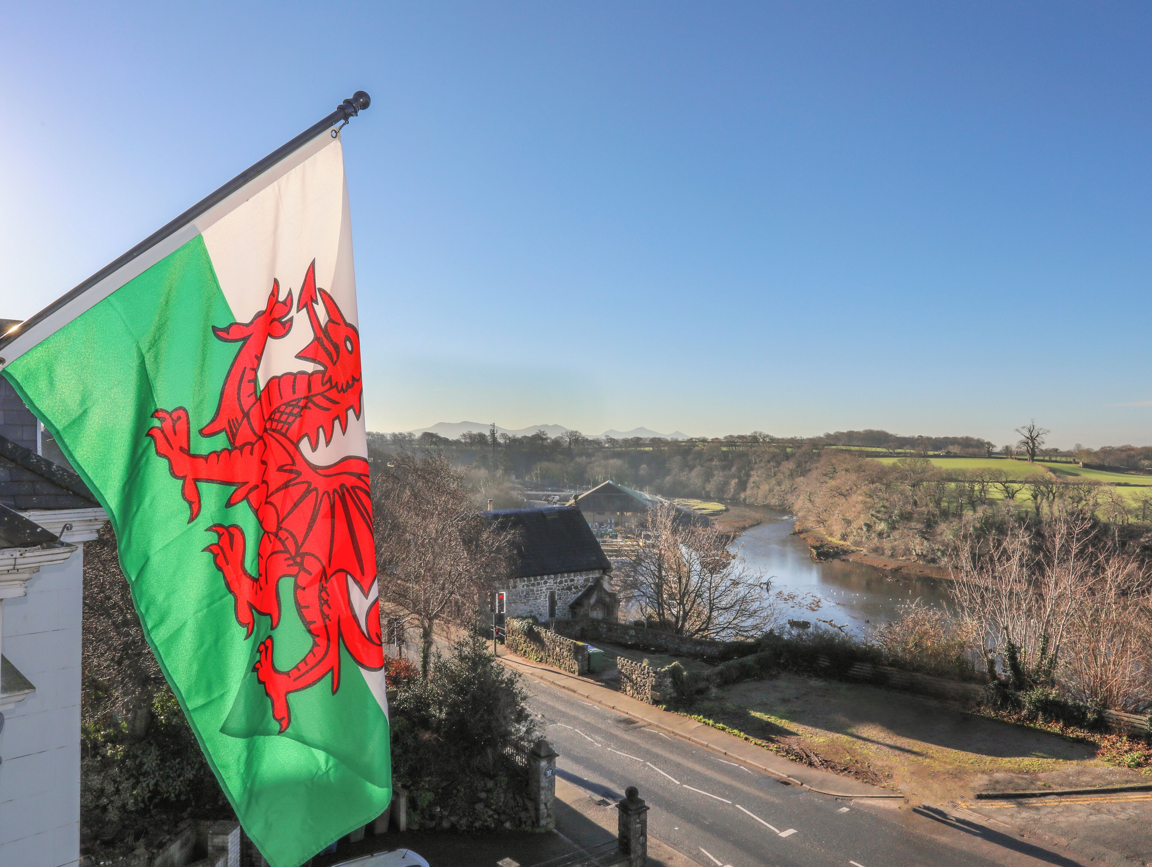 A flag with a red dragon emblem, a rural landscape with a river, and a stone building in the background.