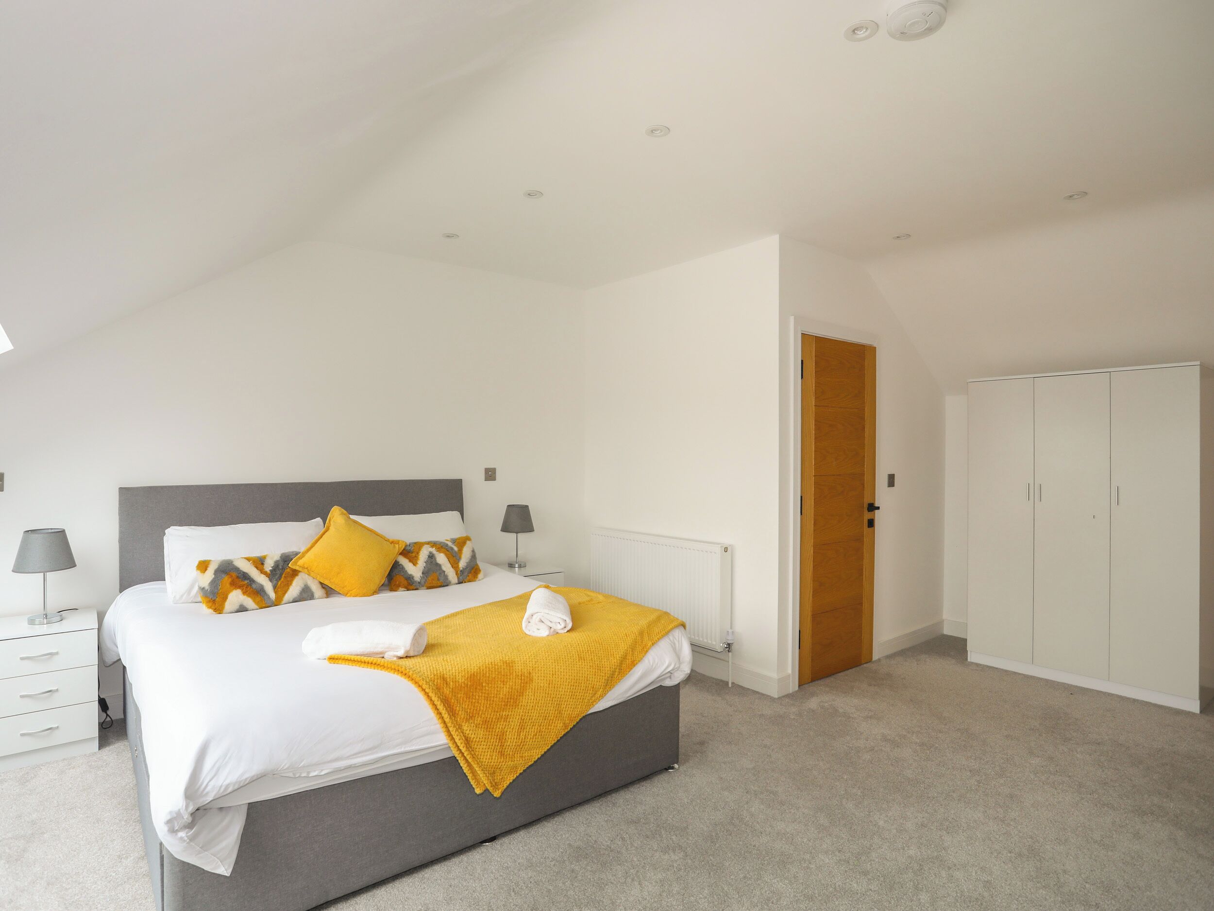 A bedroom with a bed, a bedside table, a lamp, a wardrobe, and a door.