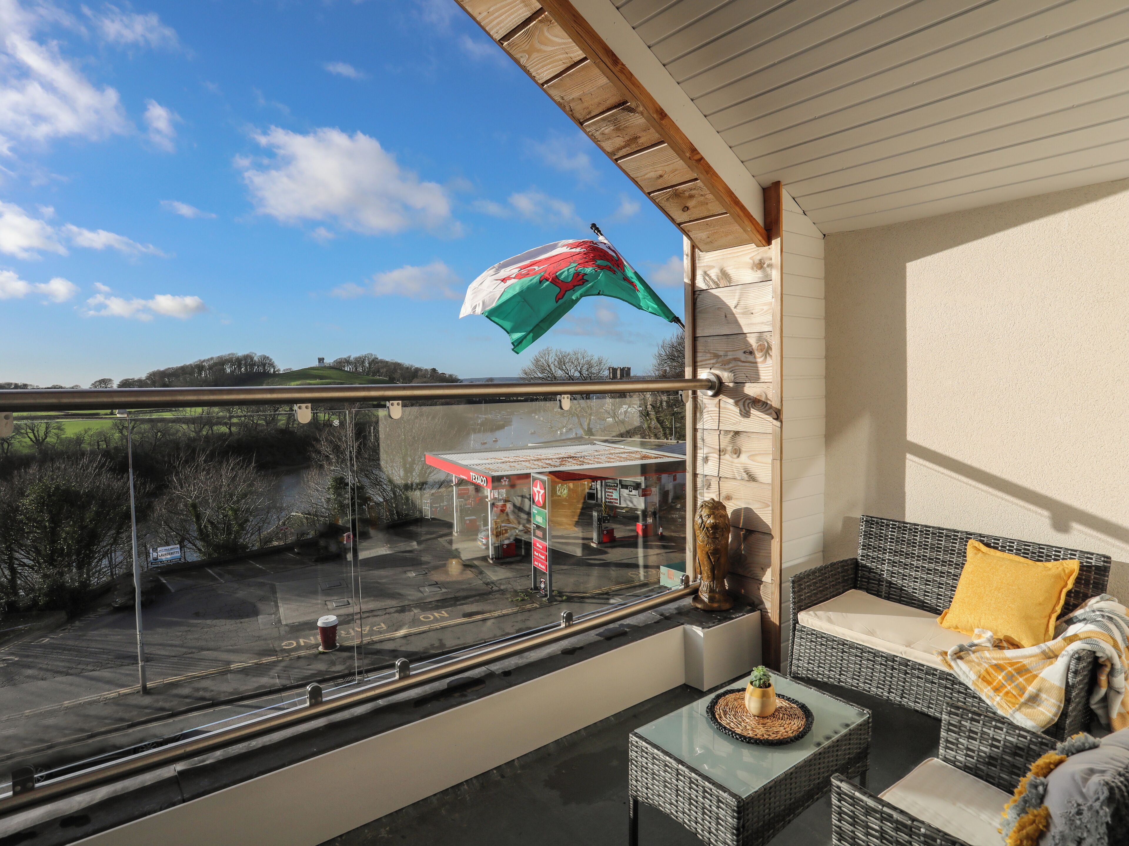A balcony with a view of a gas station, a wicker sofa, and a small table with a plant.