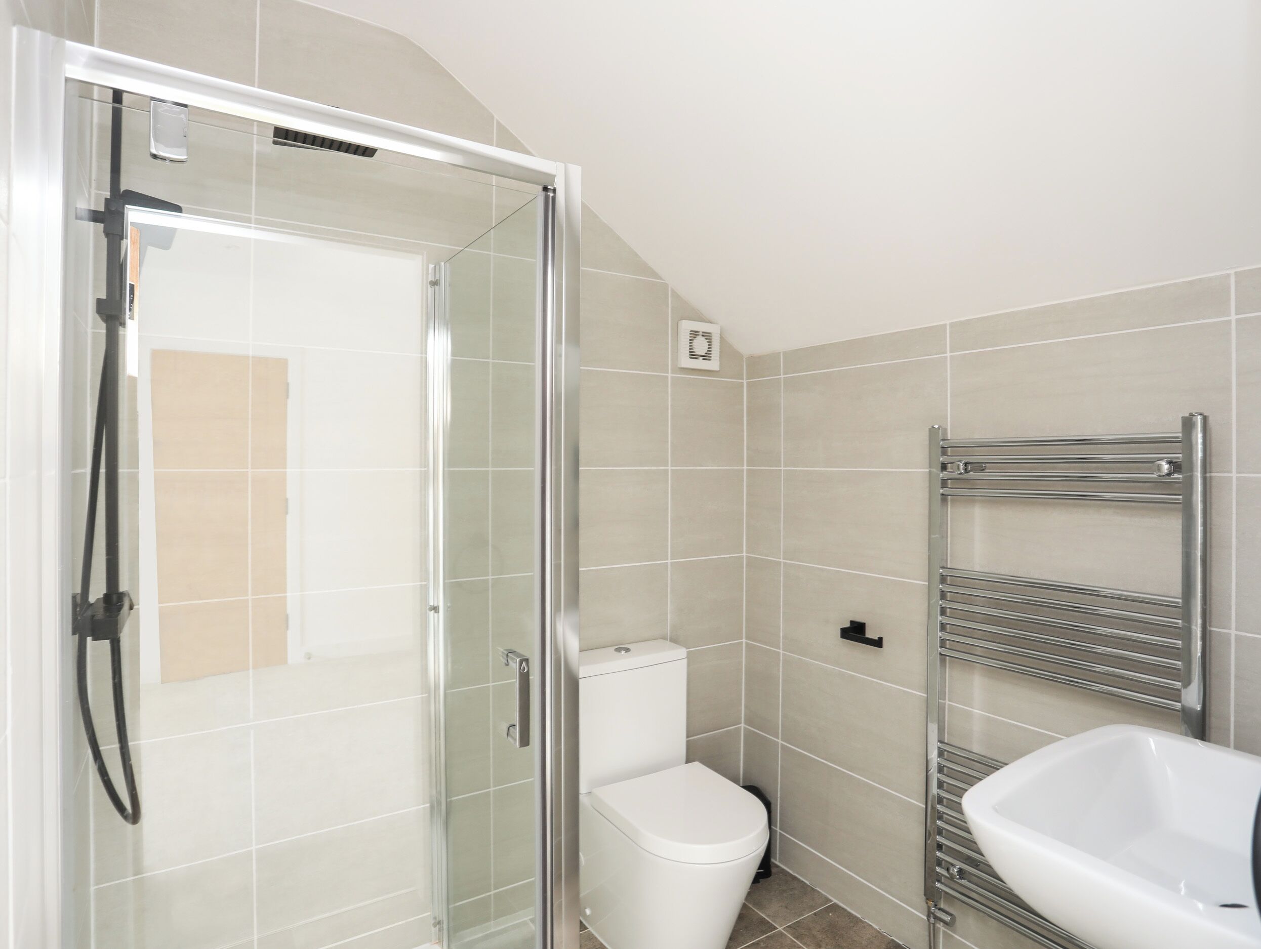 A modern bathroom with a glass shower enclosure, a white toilet, and a chrome towel rack.