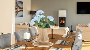 Una sala de estar moderna con chimenea, una mesa de comedor con sillas y un televisor montado en la pared.