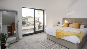 Un dormitorio con una cama grande, una puerta corrediza al balcón, un espejo y una planta pequeña.
