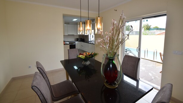 A dining area with a glass-top table, chairs, a vase with flowers, and hanging pendant lights. - Villa Machado is located in Alcantarilha with a private swimming pool. (Alcantarilha)