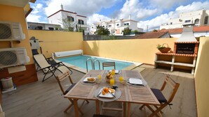 An outdoor dining area with a pool, wooden furniture, and a barbecue grill. - Villa Machado is located in Alcantarilha with a private swimming pool. (Alcantarilha)