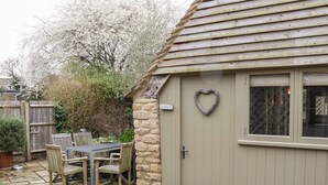 Une terrasse en pierre avec une table et des chaises, une clôture en bois et une maison dont la porte est ornée d’un motif en forme de cœur.