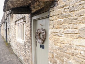 A stone building with a door, a window, and a coiled rope hanging on the door. - The Cottage and The Studio (Cirencester)