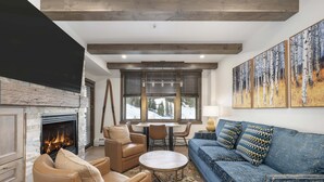 A cozy living room with a fireplace, leather sofas, a dining area, and large windows with a view of a snowy landscape.