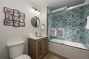Un baño con inodoro, lavabo, espejo, cuadros enmarcados y una ducha con azulejos azules.