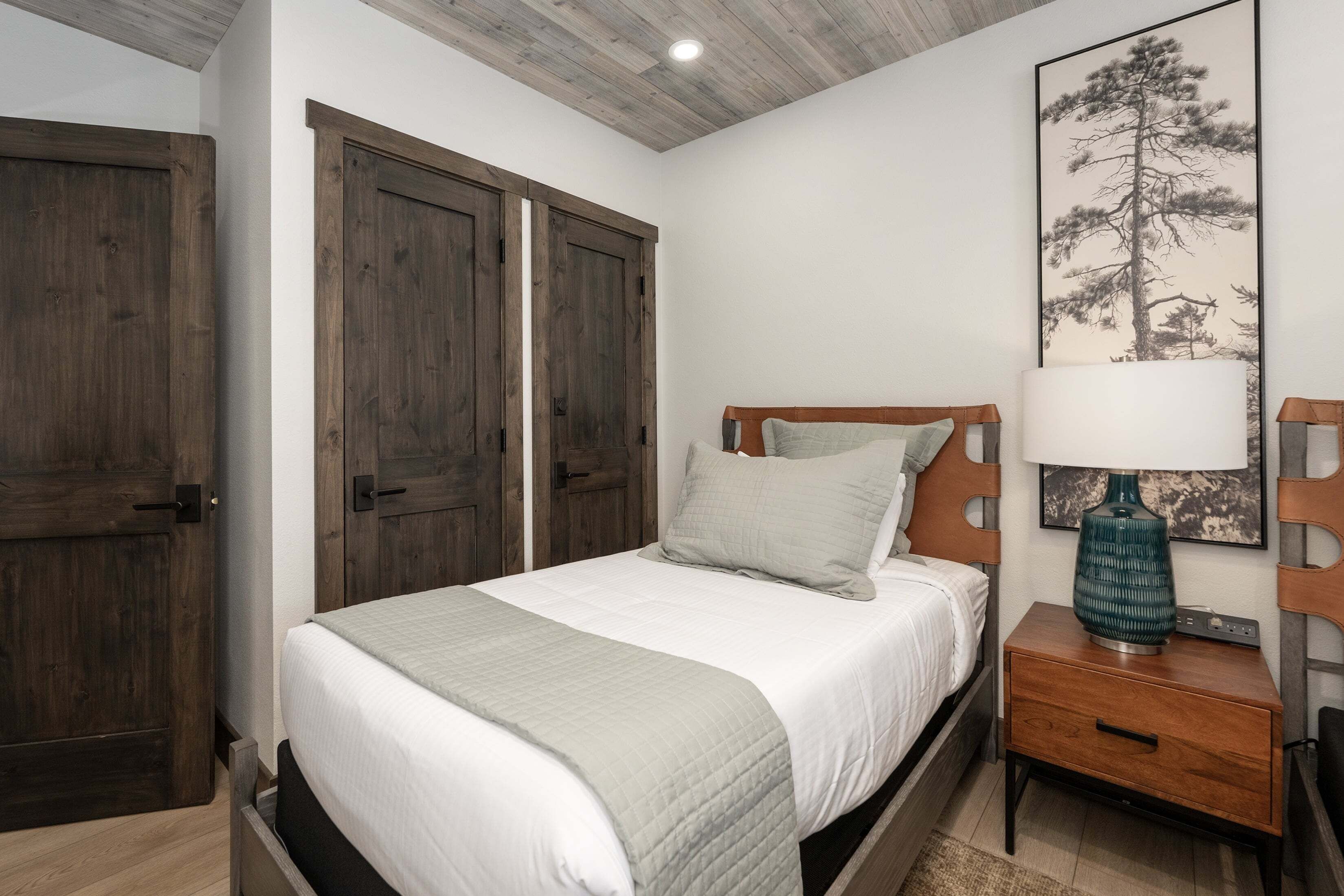 Een slaapkamer met een bed, een houten garderobe en een nachtkastje met een lamp.