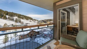 A balcony with a view of a snowy landscape, a dining area with a table and chairs, and a wooden railing.