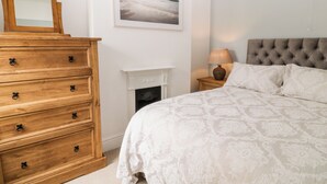 Un dormitorio con una cama grande, un aparador de madera, una chimenea y un cuadro enmarcado en la pared.