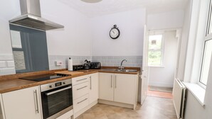 Una cocina moderna con armarios blancos, una campana extractora de acero inoxidable, horno empotrado, pileta doble y un reloj en la pared.