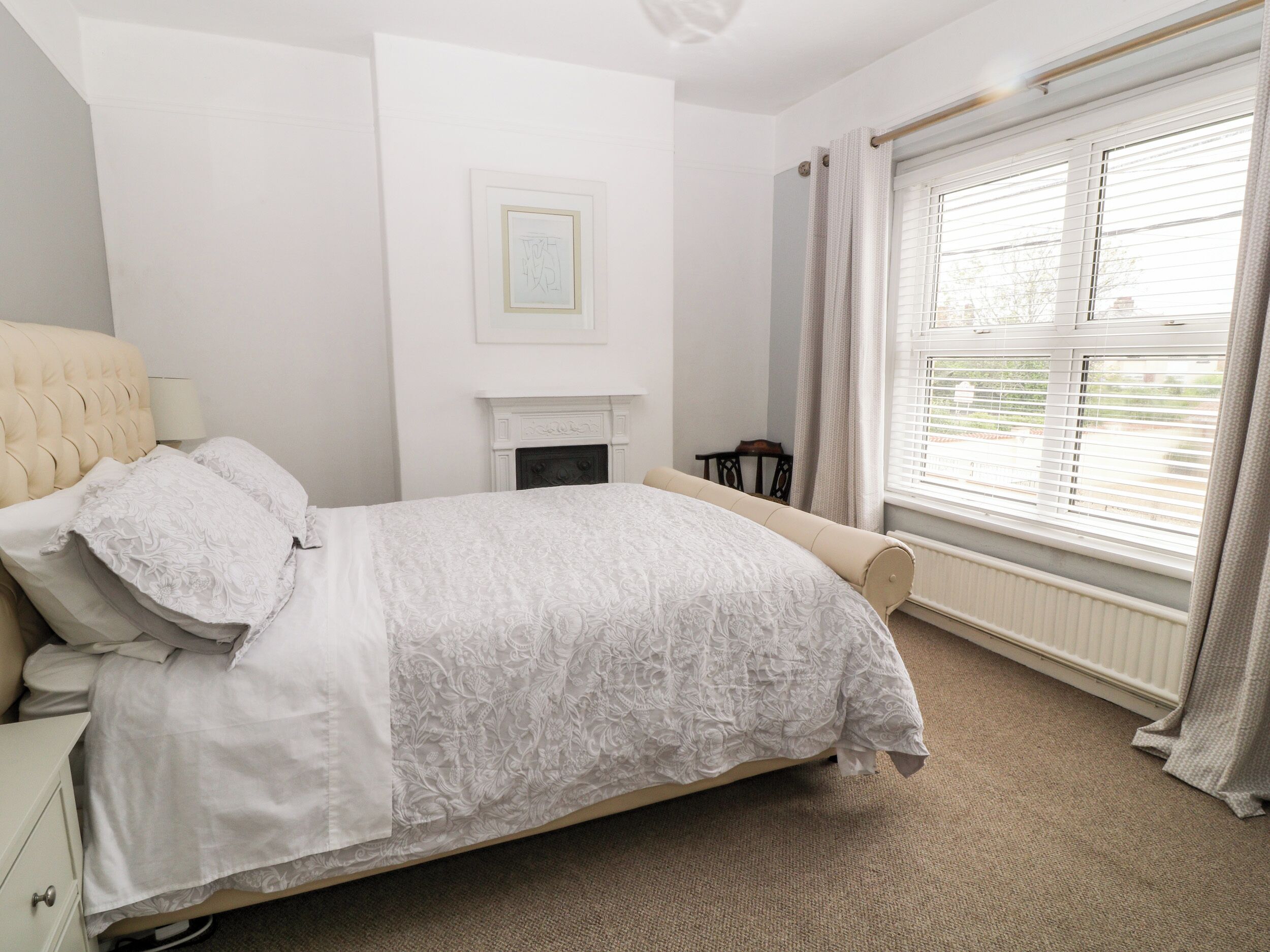 A bedroom with a bed, a fireplace, a window with blinds, and a chair.