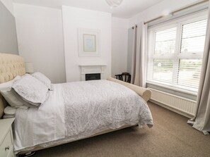 A bedroom with a bed, a fireplace, a window with blinds, and a chair. - Daisy Cottage (Bideford)