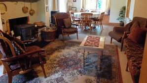A cozy living room with a fireplace, comfortable seating, a dining area, and a view of the outdoors. - Cornode Cottage (Garrykennedy)