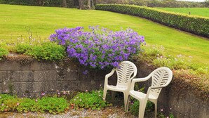 A garden with a low stone wall, two white plastic chairs, and purple flowers. - Cornode Cottage (Garrykennedy)