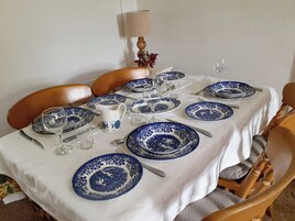 Una mesa de comedor dispuesta con platos azules y blancos, cubiertos y una jarrón.