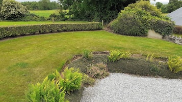 Ein gepflegter Garten mit Kiesweg, ordentlich geschnittenen Hecken und verschiedenen Sträuchern und Farnen.