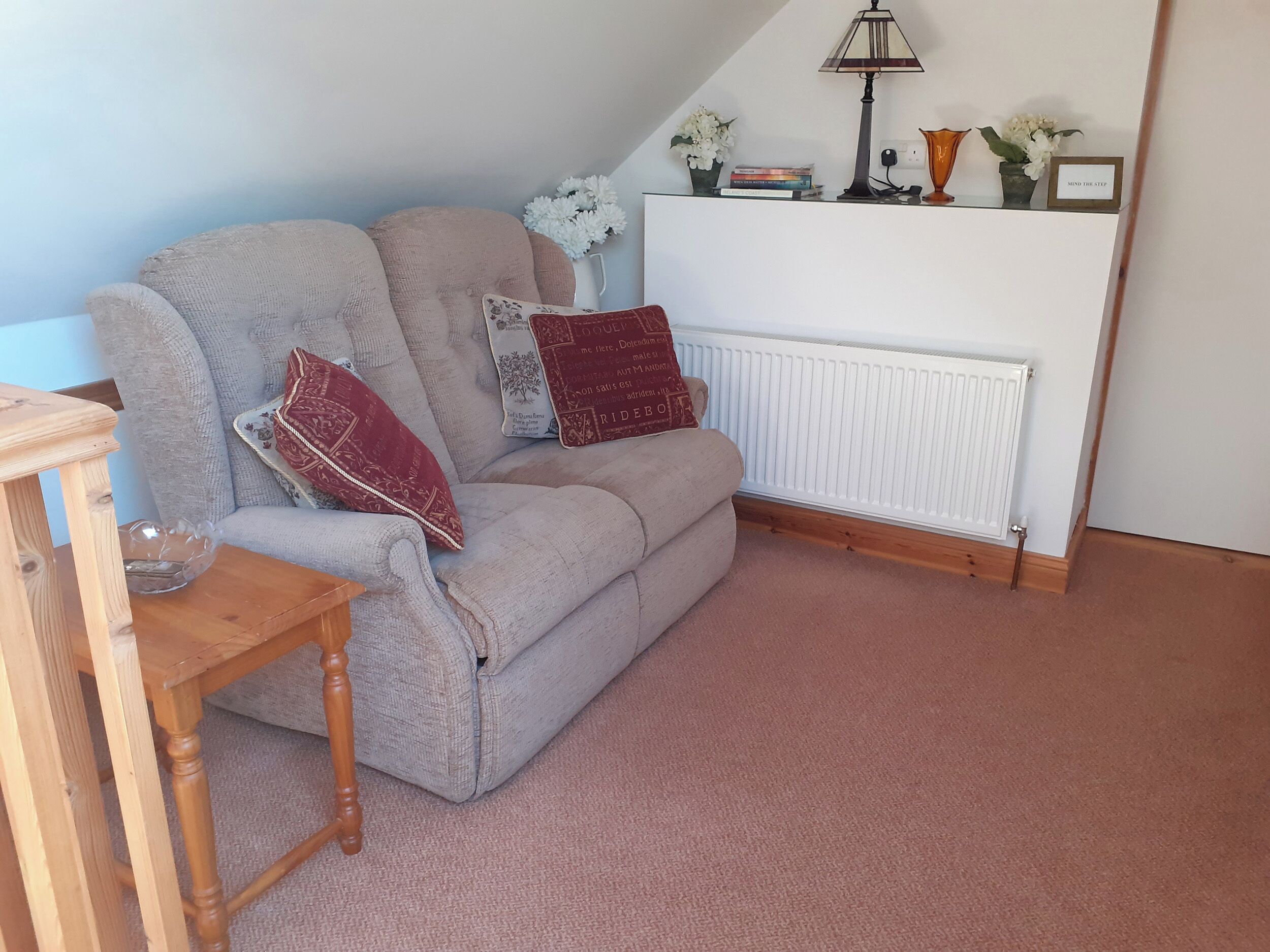 A cozy living room with a grey sofa, a wooden side table, and a radiator.